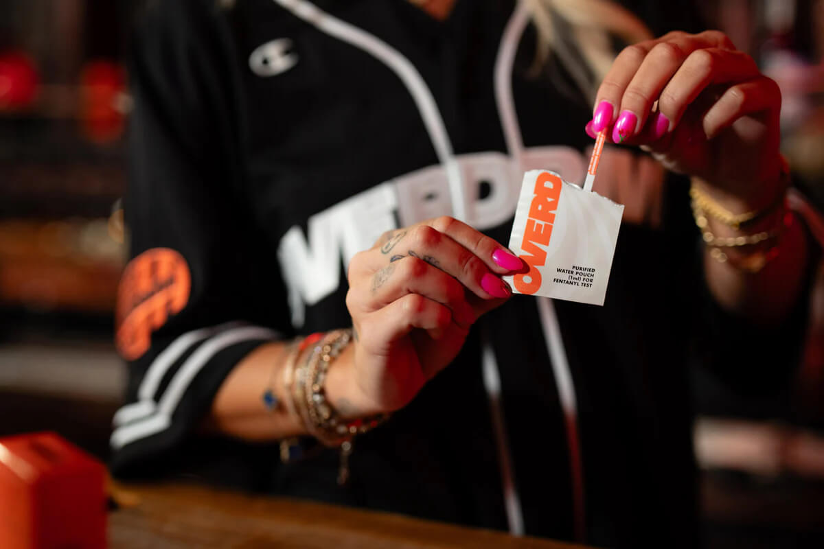 Person with hot pink nail polish dipping an Overdrive test strip into a water pouch