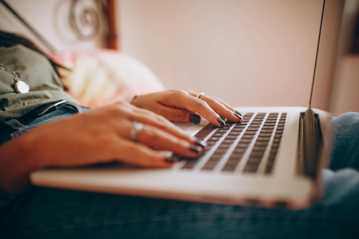 Close-up of someone's hands on a laptop keyboard, working while seated on a bed 