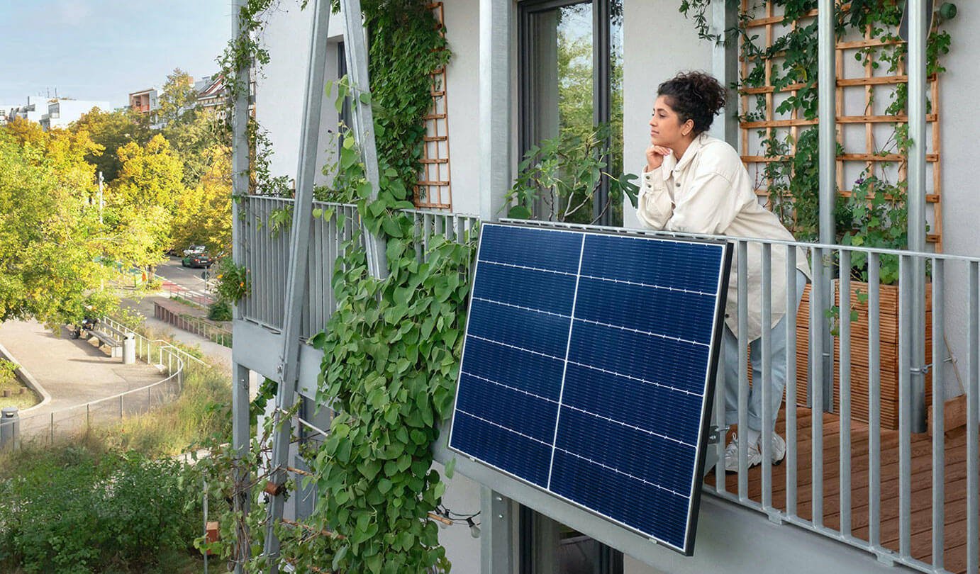 A woman leans on the railing of a balcony, attached to which is a large solar panel 