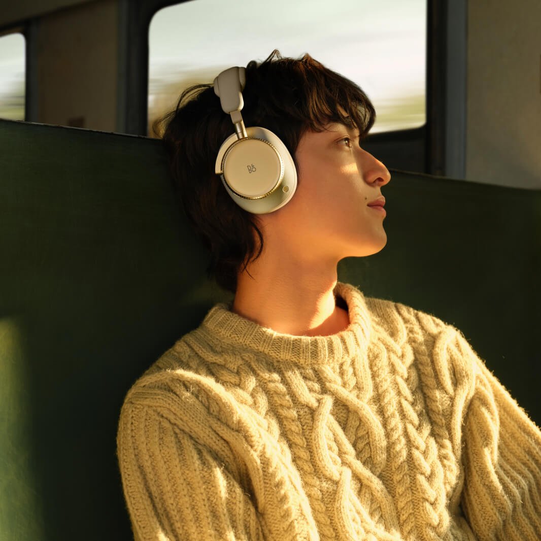 Train passenger wearing Beoplay H100 headphones and staring out the window 