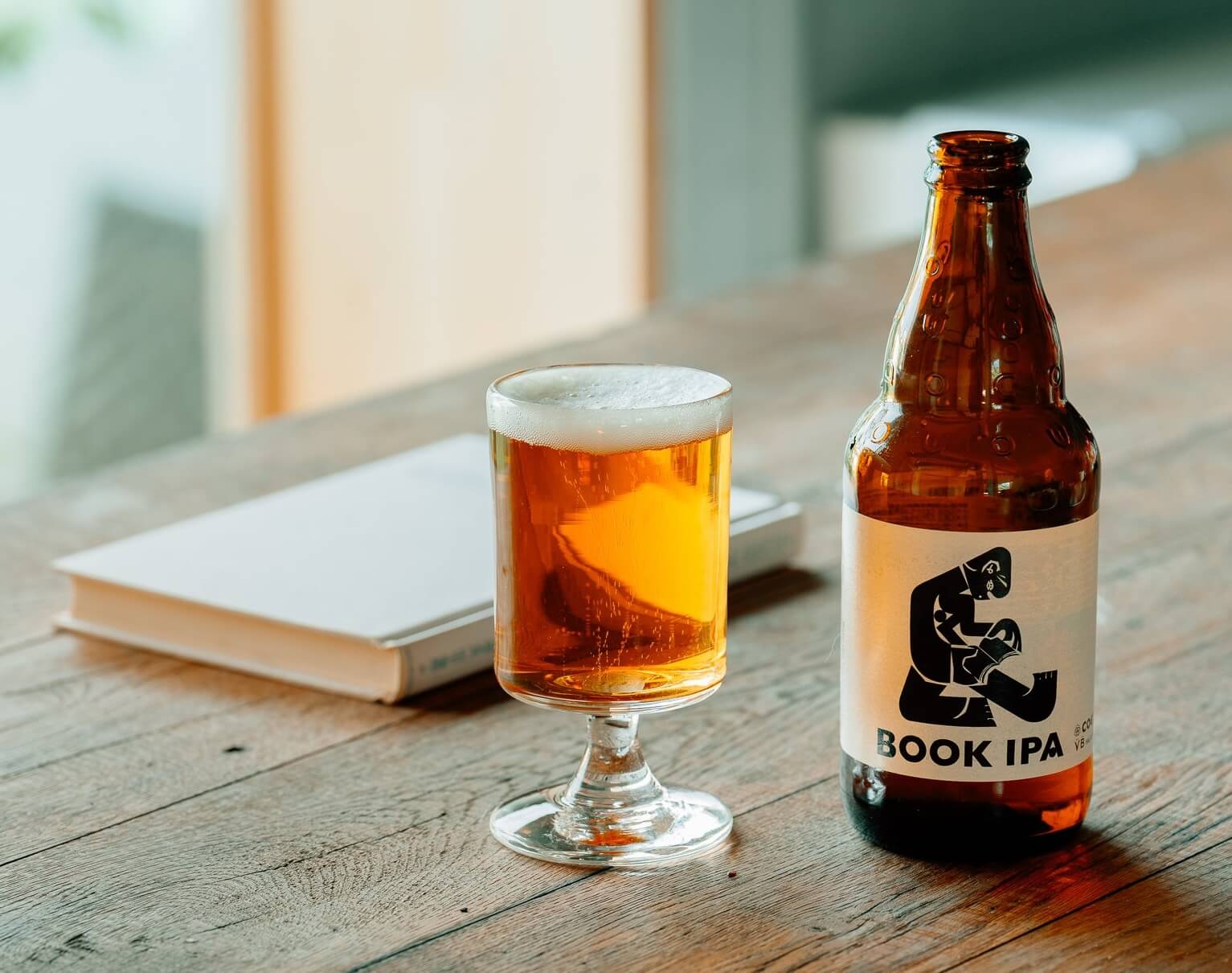 A book, a glass of beer and a beer bottle with an illustration of someone reading 