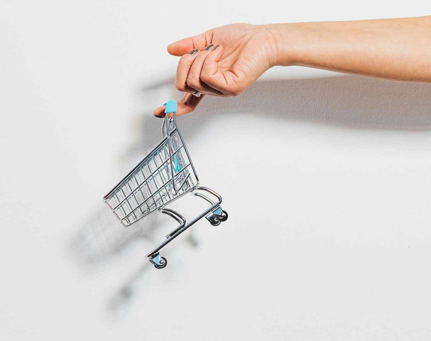 A toy-sized grocery cart dangling from an outstretched finger 