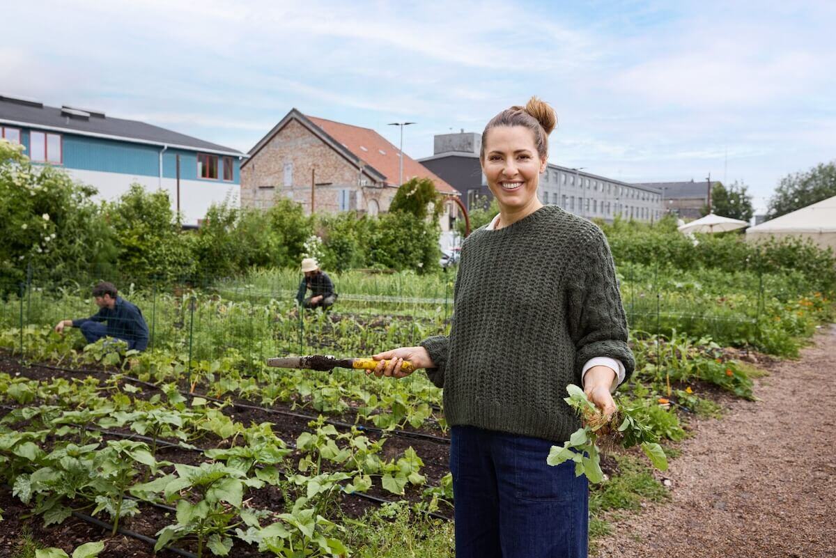 Woman on an urban farm, holding weeds and a weeding tool 