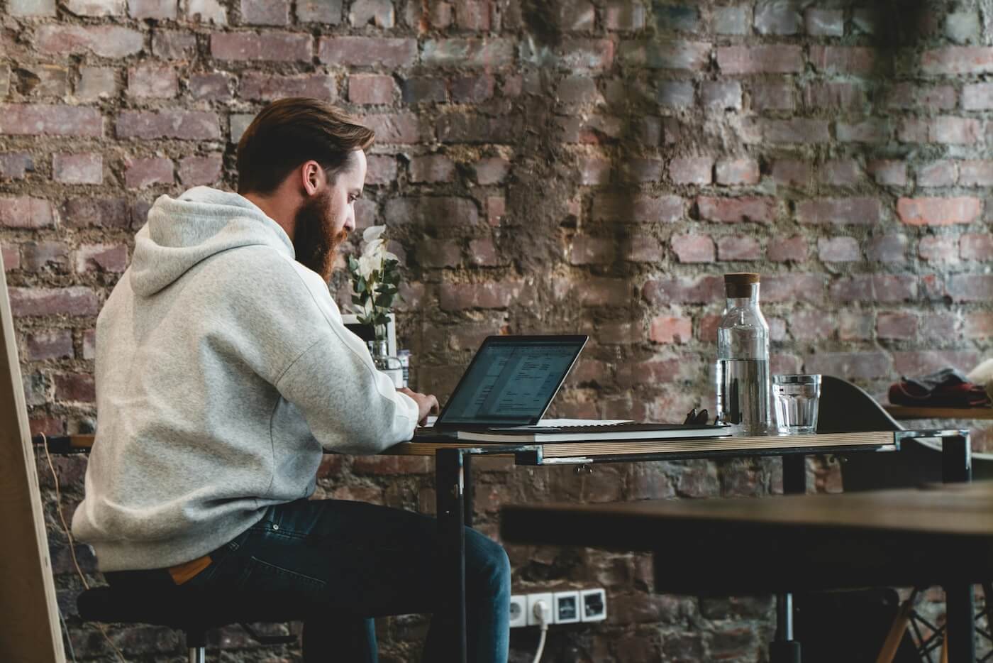 Man in hoodie working on a laptop in a third place 