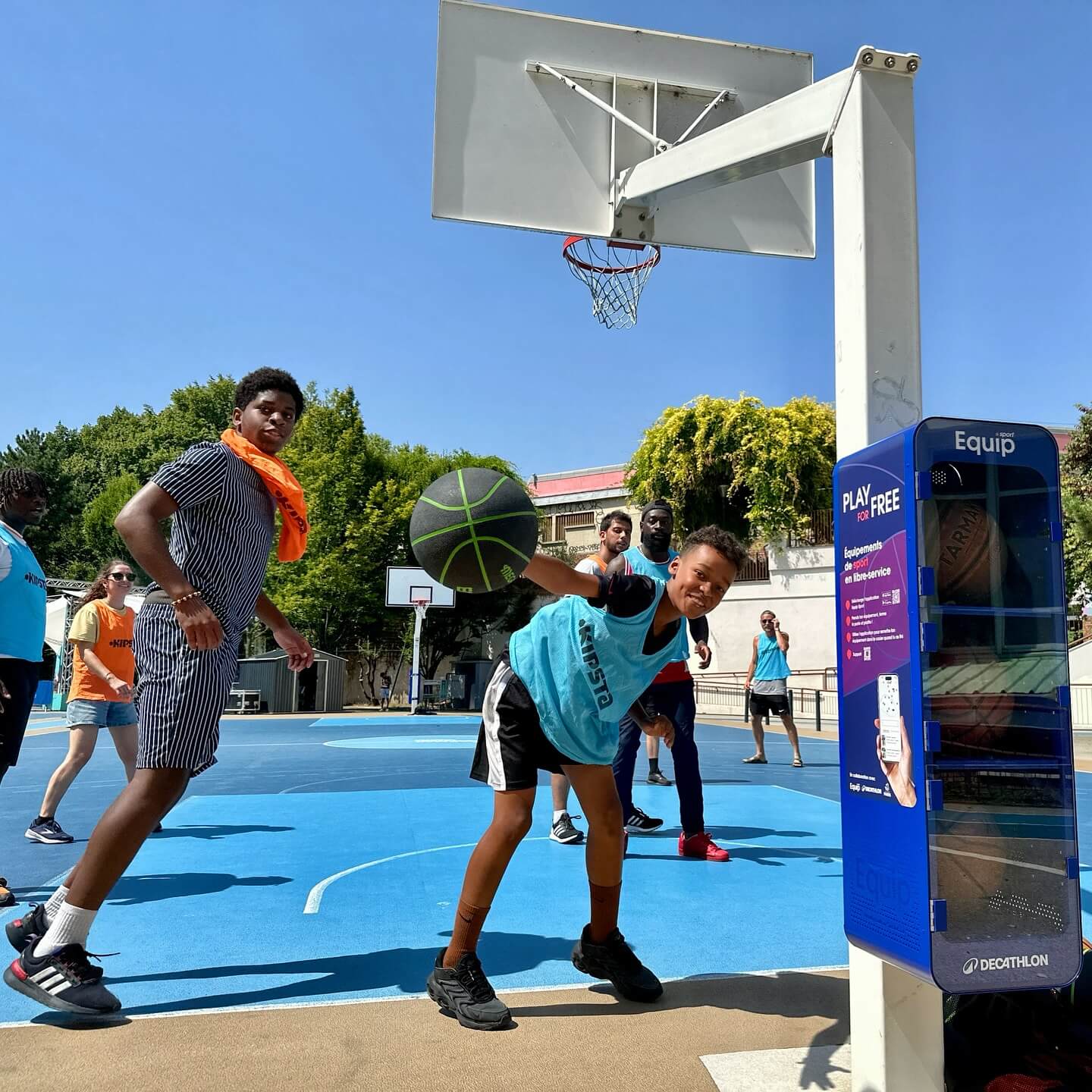 An Equip self-service rental unit by a basketball court where kids are playing 