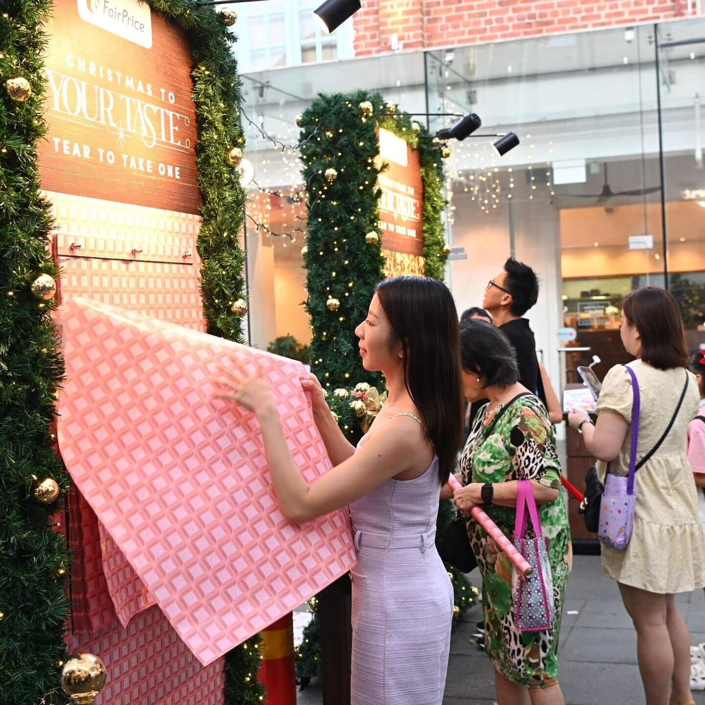 Customer tearing a sheet of scented wrapping paper off a FairPrice billboard 