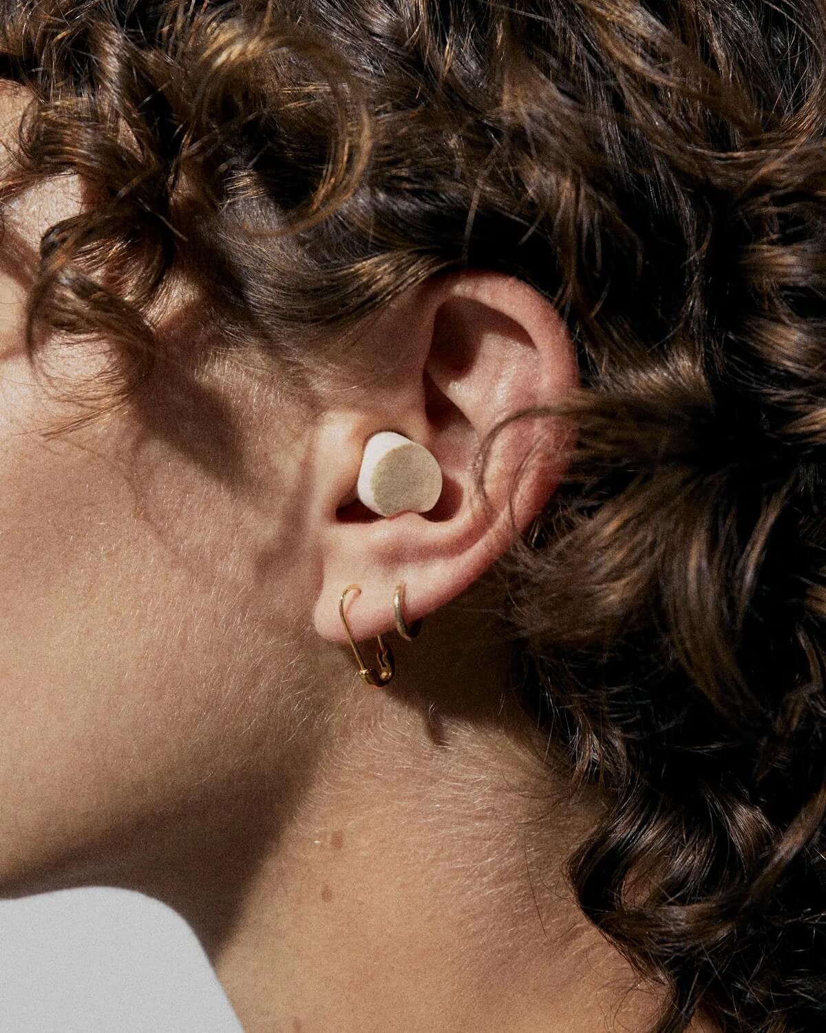 Curly-haired person viewed from the side, with an off-white mycelium foam plug in their ear 