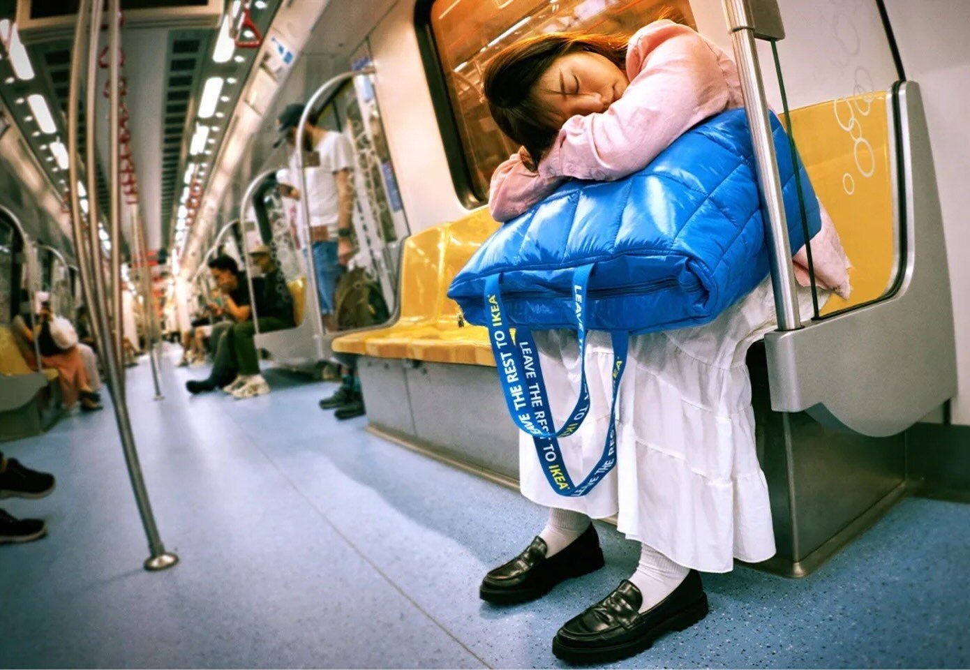 Woman on the subway, seated with her head and arms resting on a blue Ikea bag 