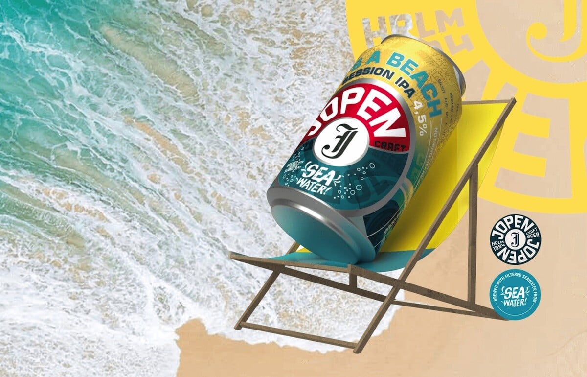 A can of Jopen beer on a beach chair, with an aerial view of waves lapping a beach in the background 