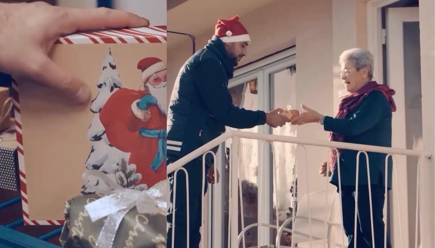 Postal worker in a Santa hat hands a gift to an older women outside her home 