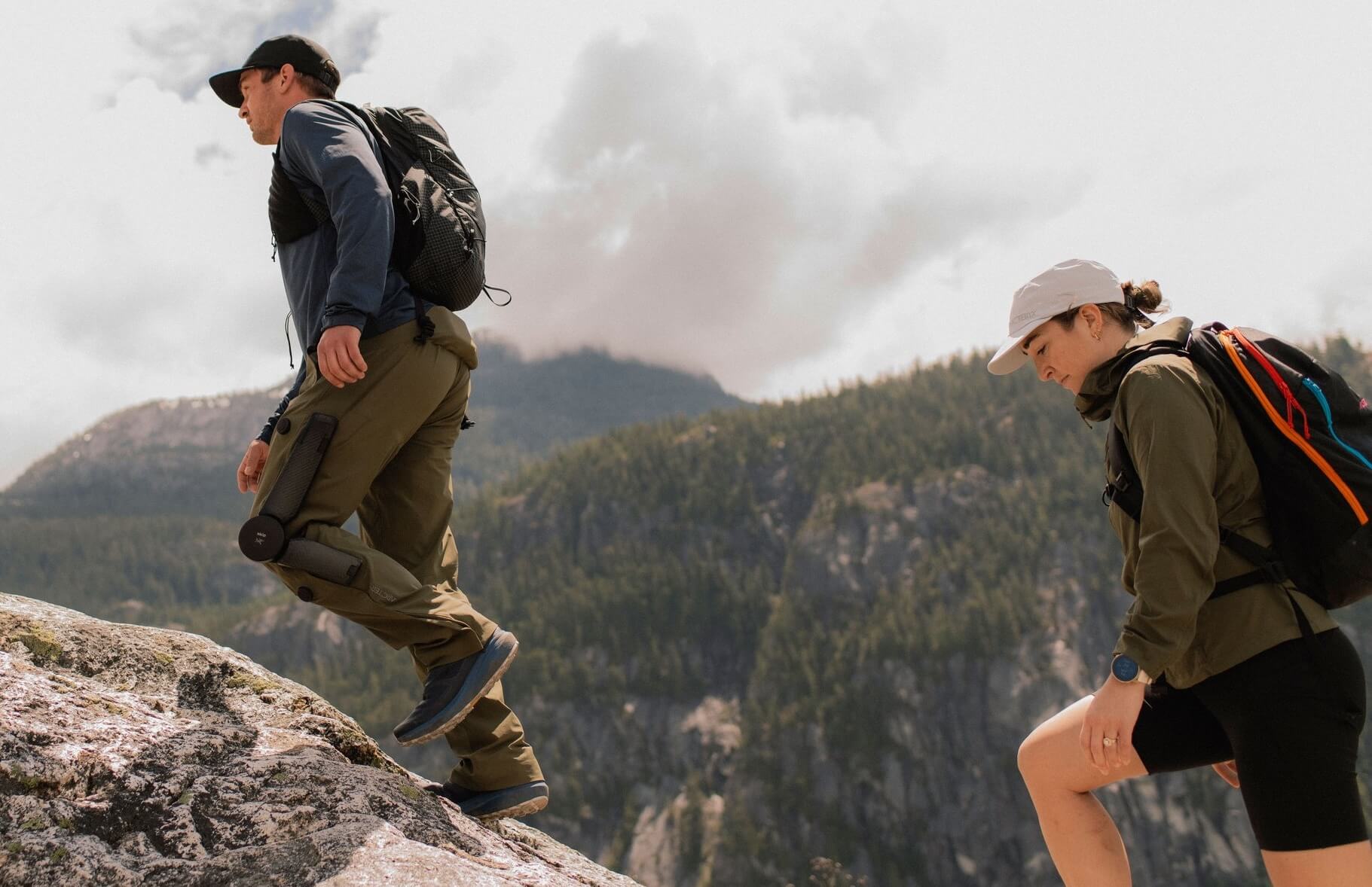 Two people hiking up a hill; one is wearing a battery-powered external knee assist 