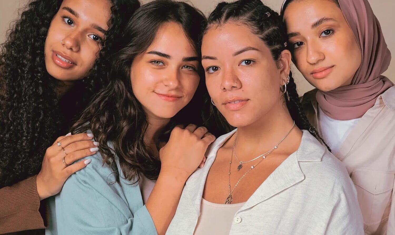 Four women leaning into each other. All have dark hair, one is wearing a headscarf 