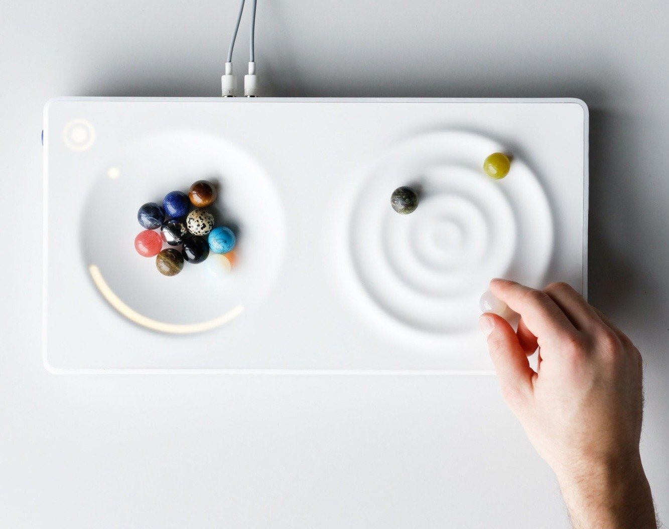 A hand placing a marble on NOISE, a white sound device with concentric rings 