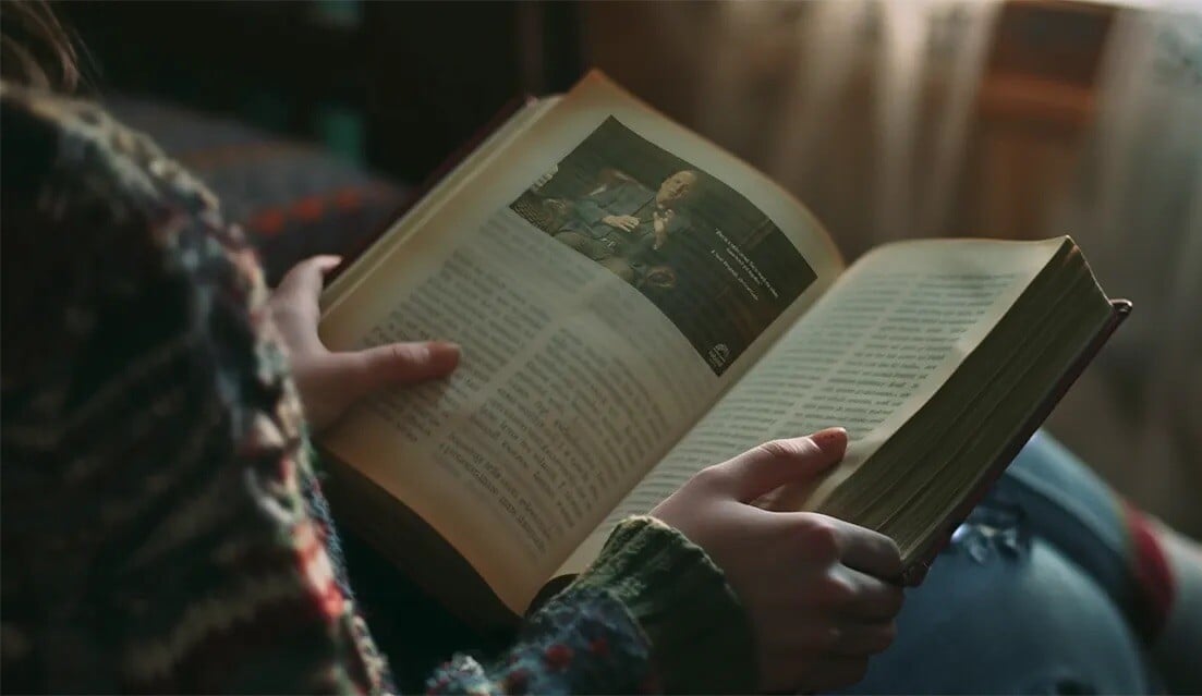 Hands holding an open book, showing a video still on the left page 
