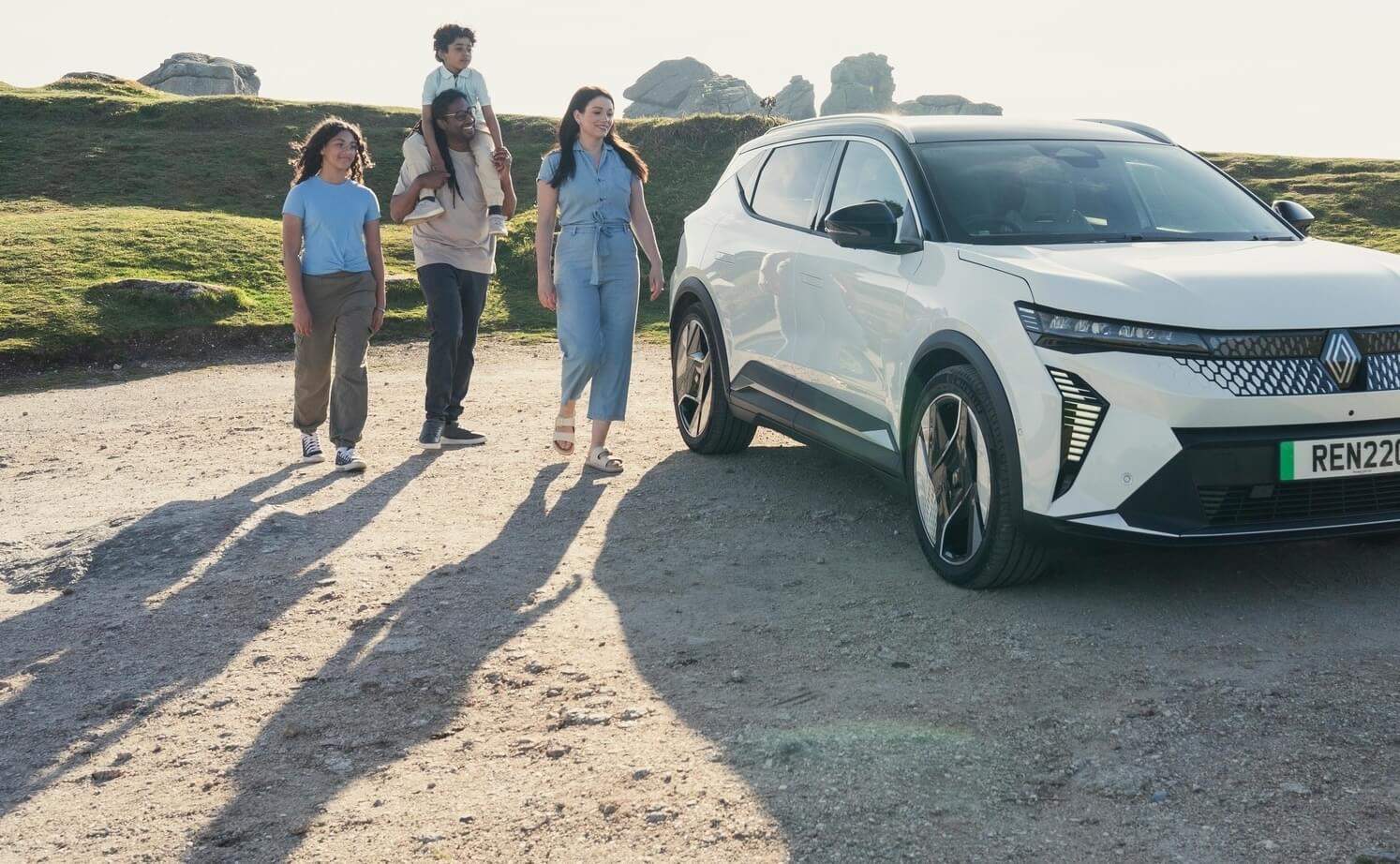 A family with two kids and a white Scenic car in a scenic landscape 