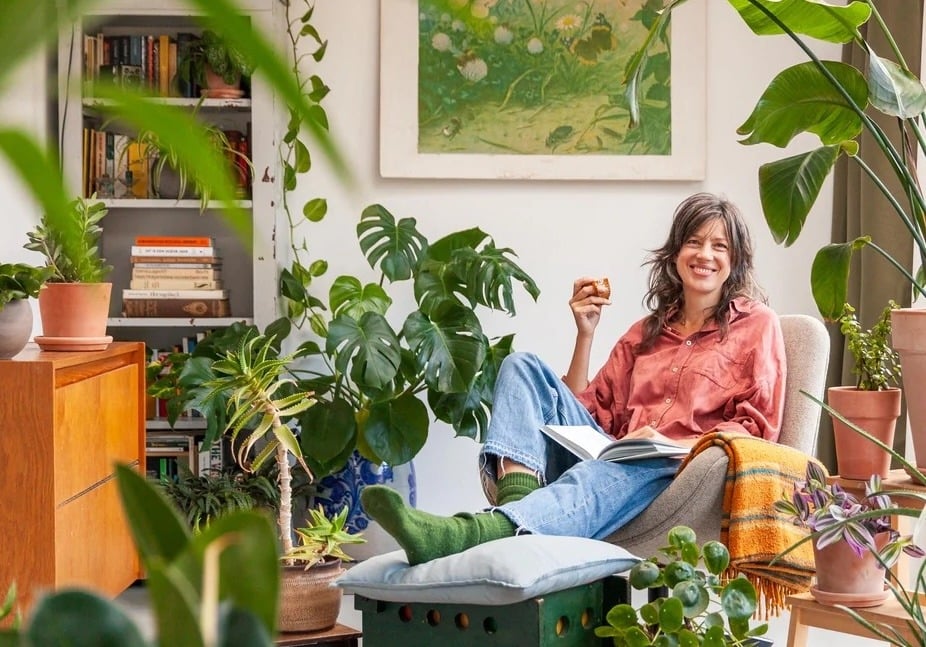 Person relaxing with a book in a living room filled with plants 