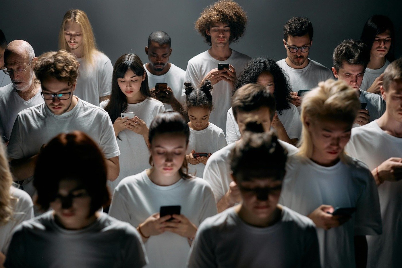 Crowd of people in white t-shirts looking down at their phones 