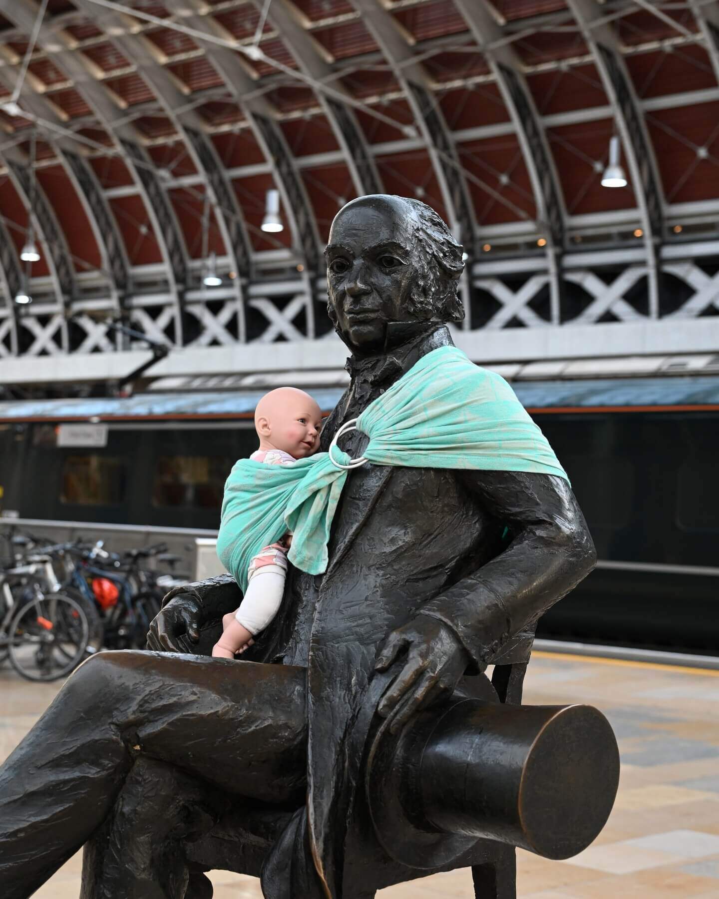 Statue of a 19th century man (Isambard Kingdom Brunel) wearing a baby doll in a turquoise sling 