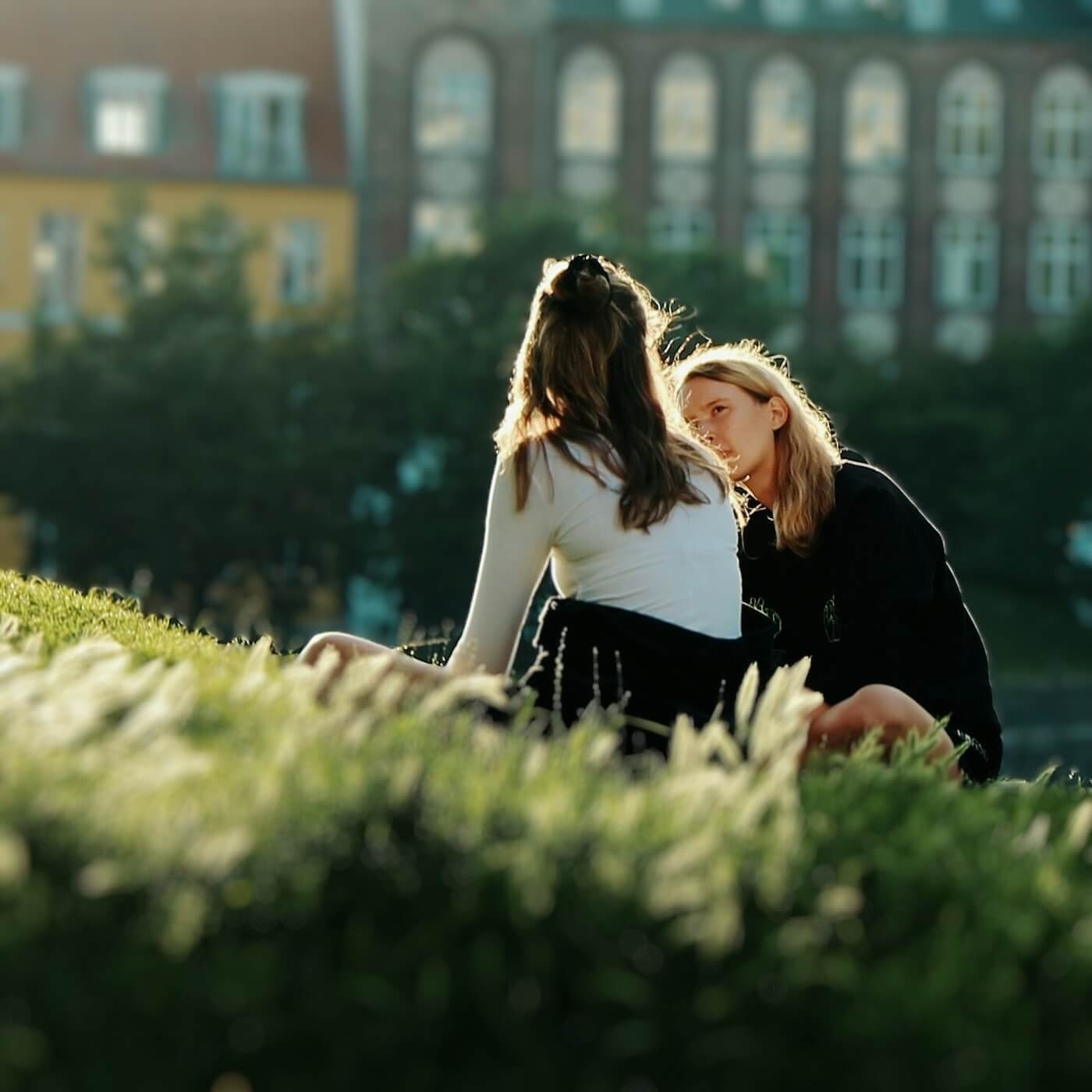 Two young women sitting outside on a grassy slope and talking 