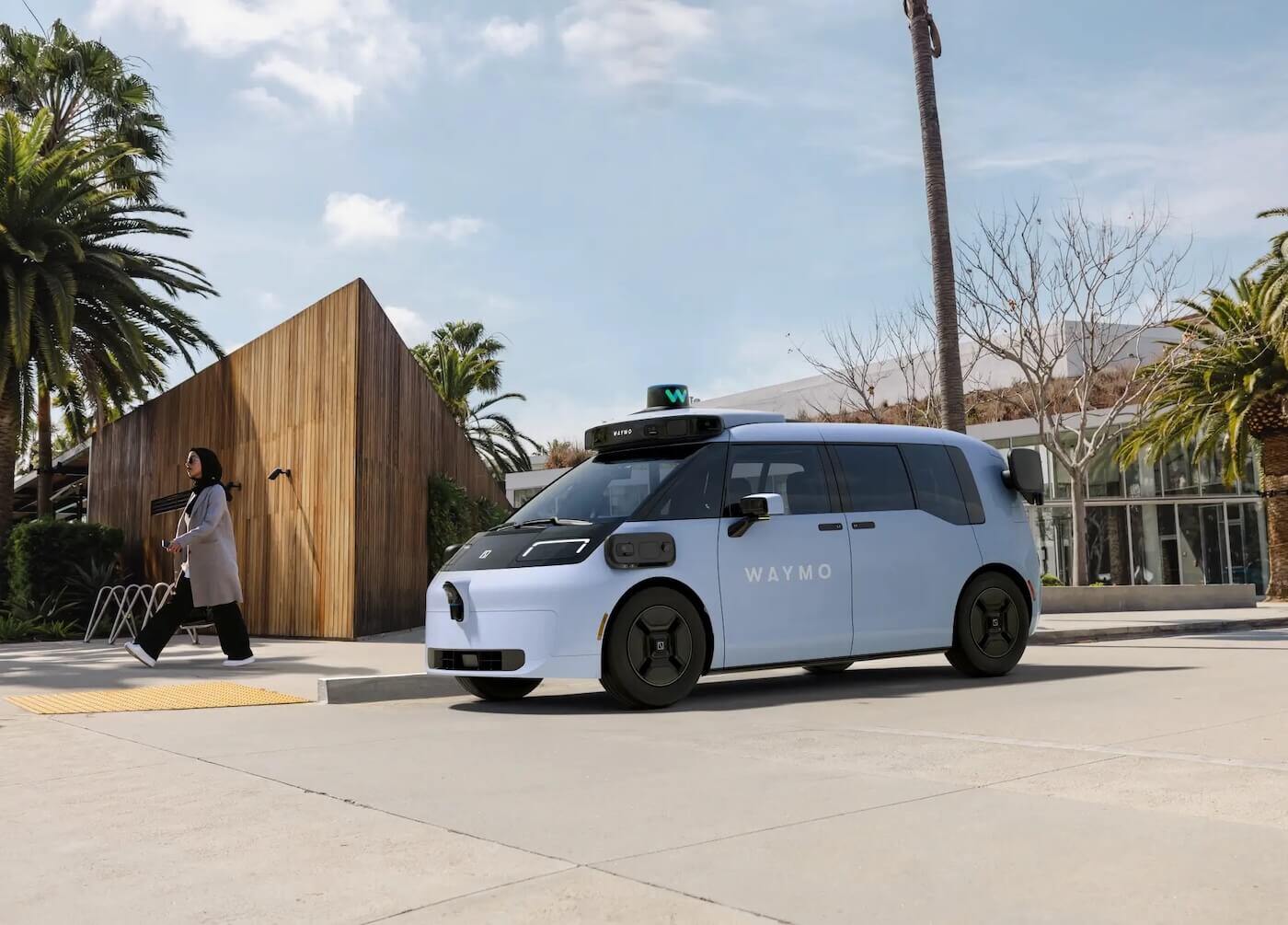 A white Waymo vehicle on a palm-lined street 